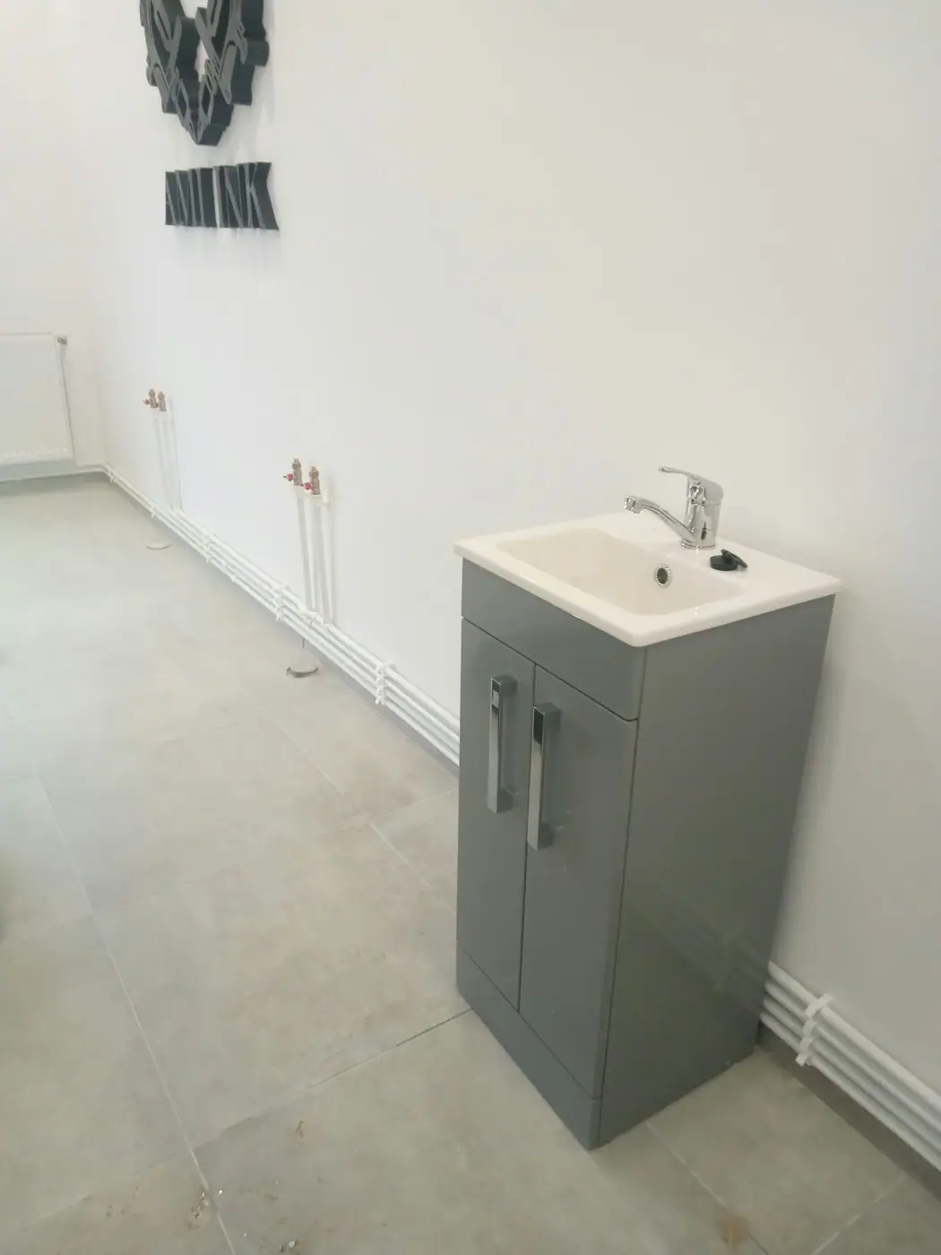 Lavoar cu baterie montat pe un mobilier gri, cu țevi de apă pe perete